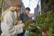 Woman in fur coat and man choosing traditional Christmas wreaths at market. — Stock Photo