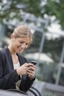Young businesswoman in black jacket using smartphone in city. — Stock Photo