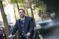 Uomo in giacca e cravatta seduto sulla bicicletta con borsa sulla strada . — Foto stock