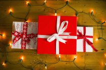 Cajas de regalo atadas con cintas rojas y luces de hadas en el suelo de madera . - foto de stock
