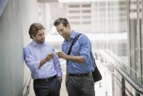 Two businessmen standing in urban street and sharing smartphone. — Stock Photo