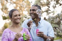 Mature couple blowing bubbles and smiling outdoors. — Stock Photo