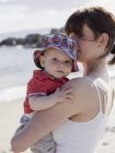 Mother holding baby son on sandy beach. — Stock Photo