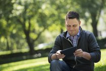 Uomo adulto mezzo utilizzando tablet digitale mentre seduto nel parco della città
. — Foto stock