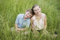 Irmão e irmã sentados lado a lado na grama alta . — Fotografia de Stock