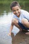 Junge im Grundschulalter pflückt Steine am Ufer des Sees. — Stockfoto