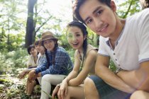 Groupe de jeunes amis asiatiques assis sur le tronc d'arbre dans la forêt . — Photo de stock