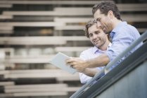 Two men standing on urban walkway and looking at digital tablet, low angle view. — Stock Photo