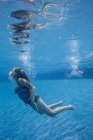 Pre-adolescent girl with fanning long hair swimming underwater in pool. — Stock Photo
