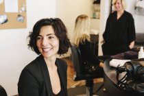 Client sitting at hair salon with people in background. — Stock Photo
