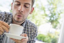 Man blowing on surface of hot coffee. — Stock Photo