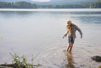 Teen girl in straw hat paddling in shallow water of country lake. — Stock Photo