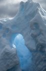 Iceberg with natural arch and translucent glow with sunlight shining through ice. — Stock Photo
