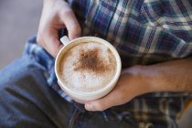 Mãos masculinas segurando xícara de cappuccino fresco . — Fotografia de Stock