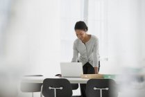 Mulher inclinada sobre a mesa e usando o computador portátil no escritório . — Fotografia de Stock