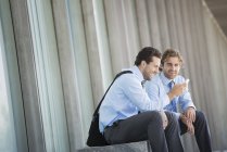 Two businessmen sitting outside office building and checking smartphone. — Stock Photo
