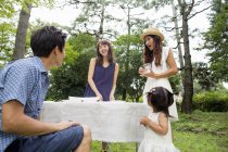 Grupo de amigos japoneses com toddler menina servindo mesa para festa ao ar livre na floresta . — Fotografia de Stock