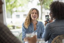 Frau spricht Bild von Freundin mit Smartphone im Café-Inneren. — Stockfoto