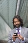 Reifer Mann im Businessanzug mit Bart und lockigem Haar nutzt Smartphone. — Stockfoto