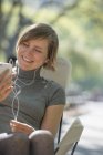 Mujer sentada en silla de camping en parque y escuchando música en auriculares . - foto de stock