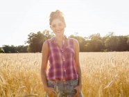 Jeune femme debout dans le champ de grandes plantes de maïs dans la lumière douce et souriante . — Photo de stock