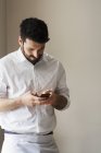 Retrato de meio comprimento de homem barbudo em avental branco usando smartphone . — Fotografia de Stock