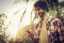 Low angle view of bearded man checking smartphone outdoors. — Stock Photo