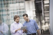 Two men standing outside building and using digital tablet together. — Stock Photo