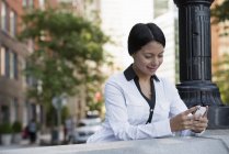 Mitte erwachsene Frau in weißer Jacke checkt Handy auf der Straße. — Stockfoto