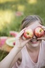 Elementary age girl holding apples in front of eyes, portrait. — Stock Photo