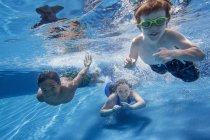 Tres niños nadando bajo el agua y sonriendo en cámara . - foto de stock