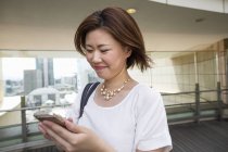 Young woman using smartphone in office building and smiling. — Stock Photo