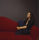 Frau in schwarzer Freizeitkleidung umarmt Knie und lehnt auf rotem Sofa. — Stockfoto