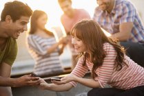 Young friends sharing smartphones on rooftop terrace party. — Stock Photo