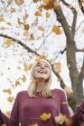 Cheerful teenage girl throwing autumnal leaves into air in park. — Stock Photo