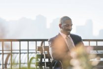 Businessman sitting on city bench, looking down and smiling. — Stock Photo