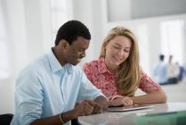 Man and woman sitting side by side and using digital tablet in office. — Stock Photo