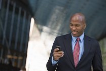 Geschäftsmann in Anzug und Krawatte lächelt und nutzt Smartphone in der Stadt. — Stockfoto