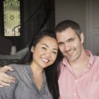 Sorrindo homem e mulher sentados dentro de casa, abraçando e olhando na câmera . — Fotografia de Stock