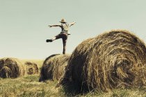 Rear view of man balancing on one leg hay bale in countryside. — Stock Photo