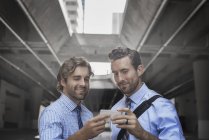 Deux hommes en chemises et cravates en utilisant smartphone avec passerelle et bâtiments en arrière-plan
. — Photo de stock