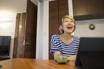Woman sitting at table with laptop computer and green tea and laughing. — Stock Photo