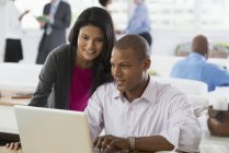 Hombre y mujer jóvenes que comparten ordenador portátil en el lugar de trabajo de oficina . - foto de stock