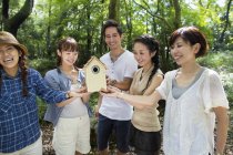 Group of cheerful friends holding wooden birdhouse in forest. — Stock Photo