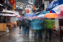 Blurred silhouettes of people with umbrellas in rain in town of Yangshuo, China — Stock Photo