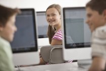 Три ребенка в школьной компьютерной лаборатории с рядами компьютерных мониторов . — стоковое фото