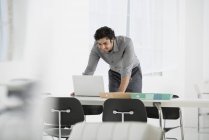 Молодой человек наклоняется и использует ноутбук в офисе . — стоковое фото