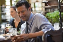 Hombre adulto medio usando teléfono inteligente mientras está sentado en el bar con amigos . - foto de stock