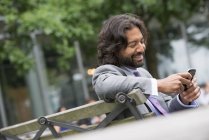 Людина в костюмі бізнес з бородою і Кучеряве волосся за допомогою телефону на вулиці лавці. — стокове фото