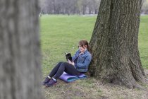 Junge Frau lehnt an Baum und liest im Central Park, New York, USA. — Stockfoto